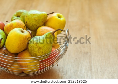 Metal basket with apples and pears on wooden table.