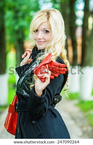 Beautiful young woman in coat and red gloves has looked back in park.