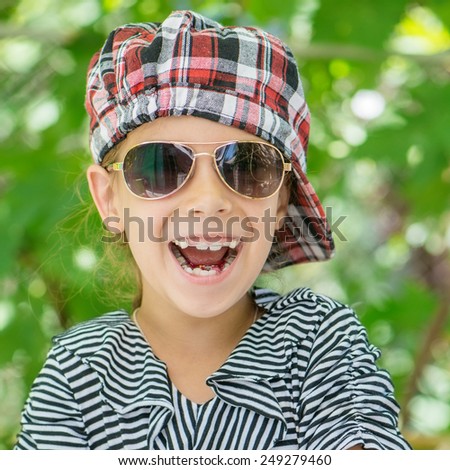 Portrait of beautiful smiling little girl with sunglasses in green summer city park.