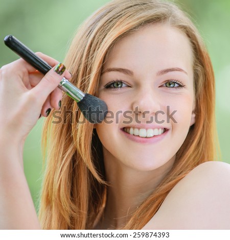 Smiling beautiful young woman with bare shoulders on face powder, against green of summer park.