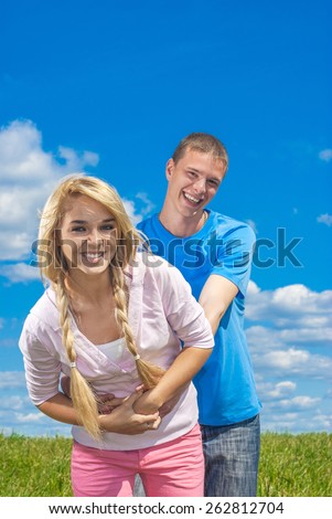 Young man hugging woman against background of green summer meadows.