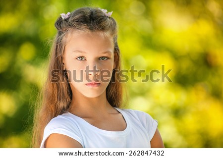 Beautiful sad teenage girl in white blouse, against green of summer park.