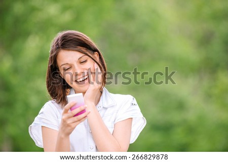 Portrait of young beautiful smiling woman wearing white blouse with mobile phone at summer green park.