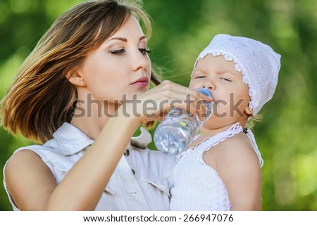 young charming caring mother gives daughter drink water bottles background summer green park