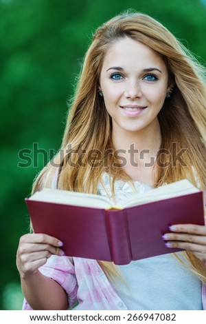 close-up of long-haired, cheerful woman is reading good book on background of summer park