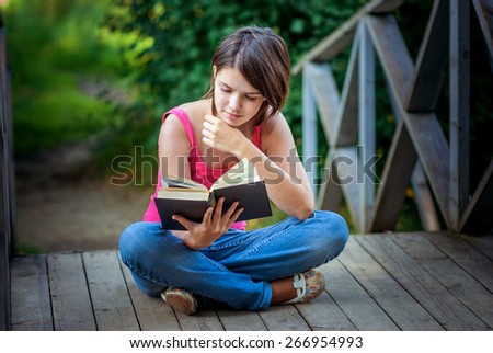 Young beautiful girl sits on bridge and reads interesting book.