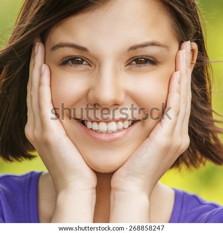 Close-up portrait of young beautiful smiling woman propping up her face in front of summer green park.