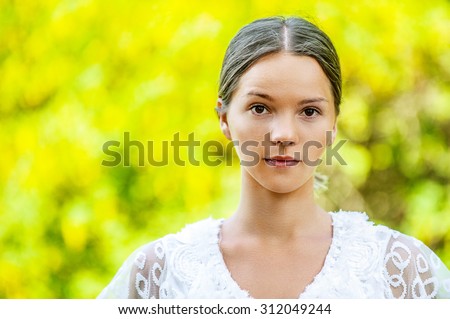 Portrait of dark-haired beautiful young woman in white blouse, against green of summer park.