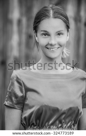 Portrait of dark-haired beautiful young woman in blouse, against background wooden fence