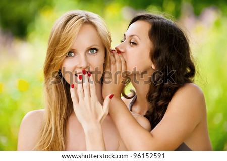 Two young beautiful women secret at summer green park
