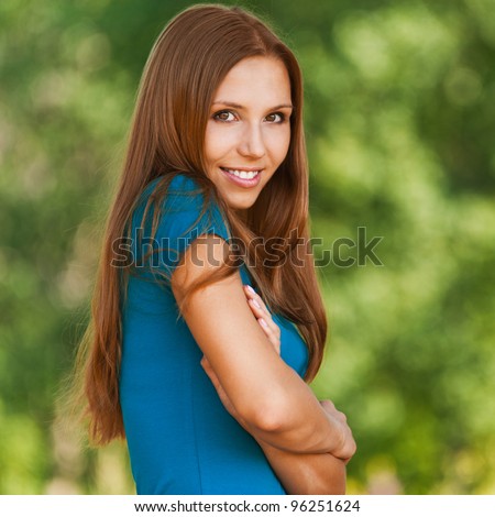 portrait of charming woman with long hair standing sideways with his arms folded across his chest and raising his shoulder background summer green park