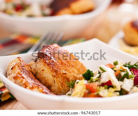 abundance of food on kitchen wooden table on napkin and fork with bowl of salad (radishes, tomatoes, parsley, eggs), meat katlety (pork, beef, lamb)