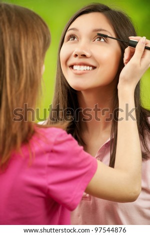 Two teenage girls dye their eyelashes background summer nature
