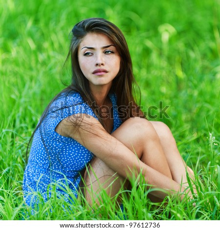 background summer green grass young charming, sad, long-haired in blue dress woman sitting hugging legs