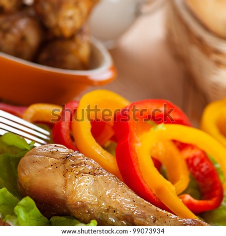 dish of fried chicken drumsticks delicious on lettuce leaves with sliced ??circles of Bulgarian pepper in background transparent glass jug with milk and wicker vase with bread