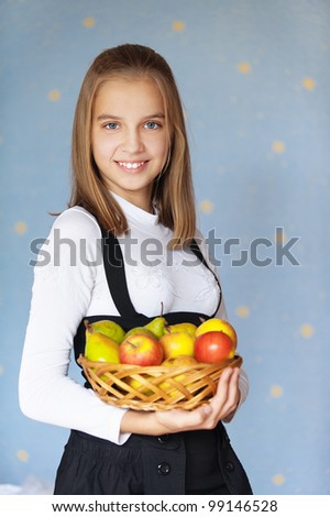 Beautiful blue-eyed smiling girl-teenager holding basket with apples, on blue background.