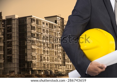 engineer holding yellow helmet for workers security on contruction background
