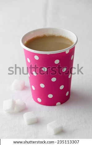 Coffee in a pink paper cup with dots pattern over white cloth