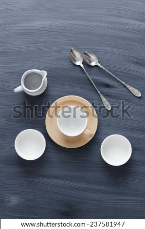 Empty coffee cups, milk jar and spoons over chalk textured table, above view