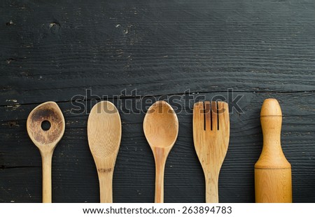 Kitchen wooden utensils over black wooden table. Horizontal and above view with copy space for text or other design