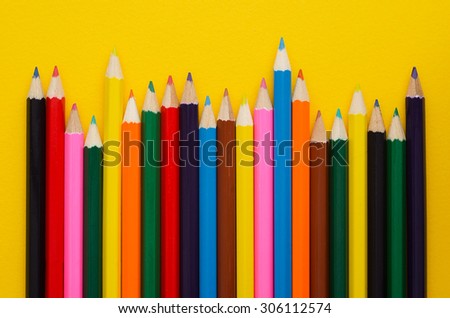 Colorful crayons organized in a row over yellow background, above view