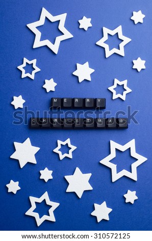 Merry Christmas text made of keyboard keys and other christmas white stars decoration over dark blue background, above view