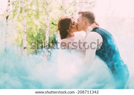 groom kissing bride in turquoise smoke on nature