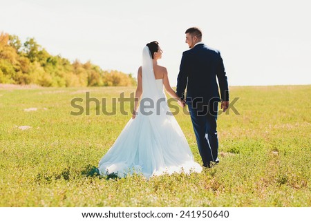happy beautiful bride and groom walking on field in sunlight