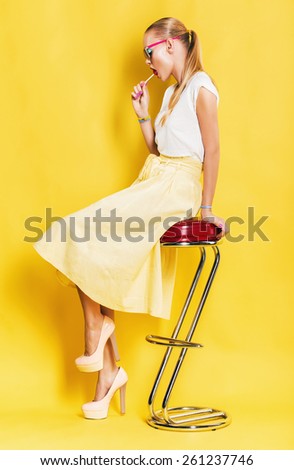 sexy woman in yellow skirt with lollipop sitting on chair on yellow background