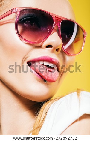 woman in pink sunglasses showing tongue on yellow background