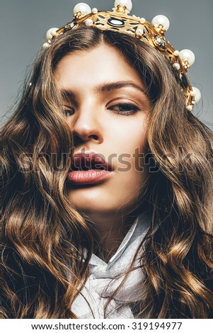 beautiful woman with curly hair in golden crown in studio