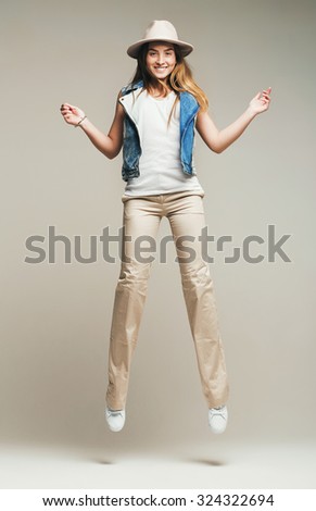 smiling woman jumping in pants and denim waistcoat in studio