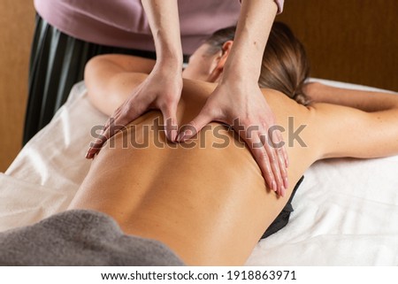 Relaxed young woman having healing body massage. Female therapist rubbing lady's back, giving her relaxing massage. Close-up of the masseuse hands doing back massage. Body care, massage, spa concept.