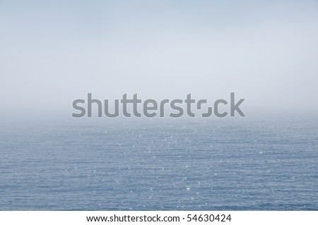 Fog in the middle of the blue ocean and some sparkling reflections shining through  it.