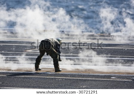 Flight line crewman checks the catapult tracks in-between launches aboard a US aircraft carrier.\
\
\
\
This photo is represented on my website: http://www.artistovision.com/military/carrier-crewman.html