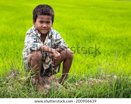 Siem Reap, Cambodia - December 25, 2013: An unidentified Cambodian boy posing for a portrait sitting on a rice field near Siem Reap, Cambodia.