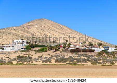 Holiday houses village on beautiful Sotavento beach on southern coast of Fuerteventura and volcano mountain in the background, Canary Islands, Spain
