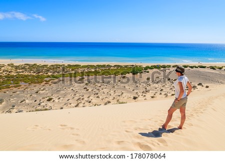 Young attractive woman standing on sand dune on Sotavento beach on Jandia peninsula and looking at ocean, Fuerteventura, Canary Islands, Spain