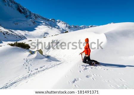Young woman tourist in red jacket holding ice-axe in fresh snow looking at winter panorama of 5 lakes valley, High Tatra Mountains, Poland