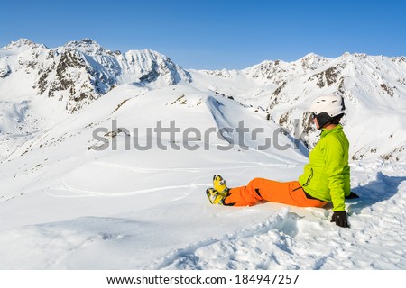 Young woman alpine skier sits in snow after reaching summit and looks at mountain peaks of Austrian Alps, Riffelsee Pitztal.