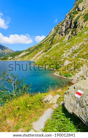 Red mountain trail sign on a rock near mountain lake Czarny Staw on sunny summer day, High Tatra Mountains, Poland