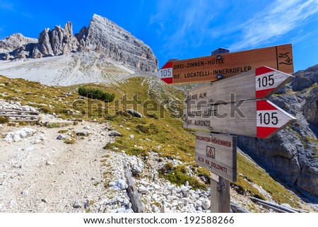 Sign in focus on hiking path with blurred view of Tre Cime di Lavaredo famous rock formation, Dolomites Mountains, Italy