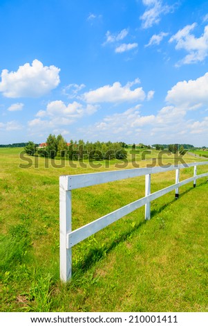 White fence on green field with white clouds on blue sky near golf club area on sunny summer day, Poland