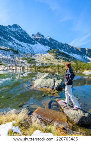 Young woman tourist looking at mountains and standing on a rock in alpine lake, Gasienicowa valley, High Tatra Mountains, Poland