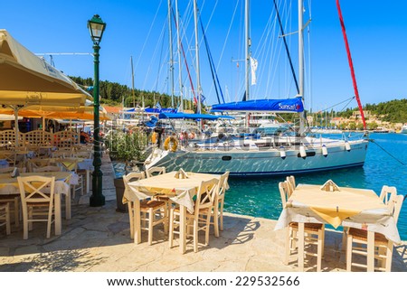 FISKARDO PORT, KEFALONIA ISLAND, GREECE - SEP 16, 2014: restaurant tables in typical Greek tavern and yacht boats in Fiskardo port. This town is most visited tourist destination on the island.