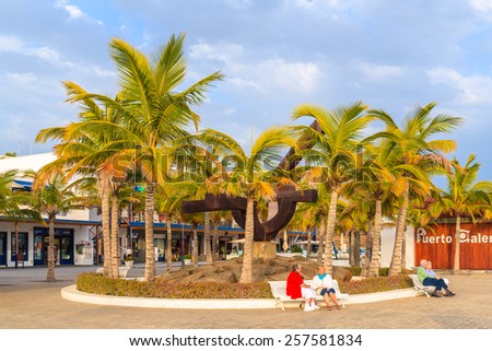 PUERTO CALERO MARINA, LANZAROTE ISLAND - JAN 12, 2015: square with palm trees and people sitting on bench in Puerto Calero port built in Caribbean style. This is a modern yacht marina.