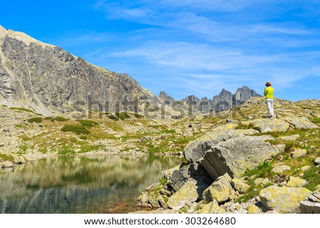 Young woman tourist standing on top of a rock on shore of alpine lake in summer landscape of Starolesna valley, High Tatra Mountains, Slovakia