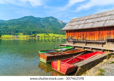 Two colorful fishing boats and wooden cabin on shore of Weissensee lake in summer landscape of Carinthia land, Austria