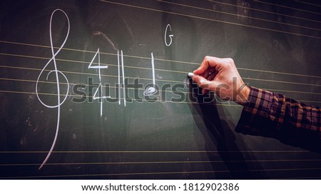 Hand writing music notes on a score on blackboard with white chalk. Musical composition or training or education concept.