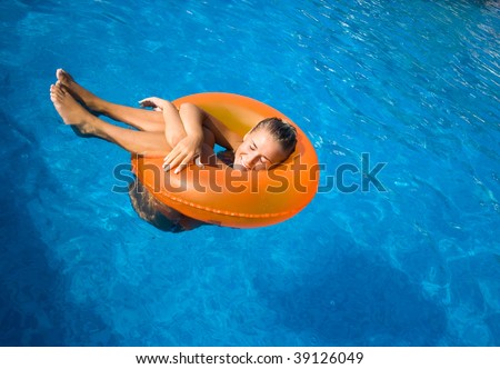Beautiful blonde girl swimming in hotel pool on inflatable raft